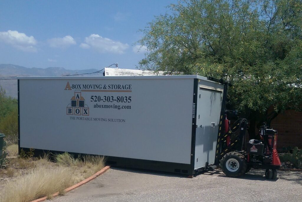 A storage container for home moving labeled "A-Box Moving & Storage" sits on a driveway next to a small forklift.